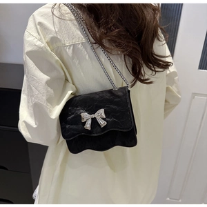 Vue détaillée du sac bandoulière plissé noir avec nœud argenté sur un mannequin