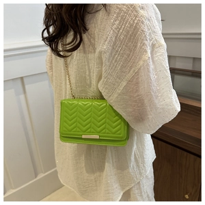Detail of green quilted crossbody bag with gold chain strap on model's shoulder
