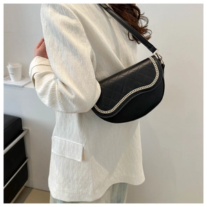Bolso de hombro negro acolchado con cadena dorada lucido sobre una chaqueta blanca chic