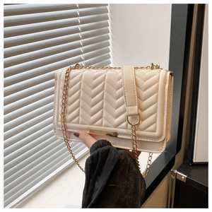 Detail of white quilted handbag with golden chain strap and rectangular metal clasp