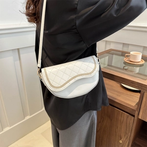 Sac selle crème matelassé avec chaîne dorée porté par un mannequin en intérieur chic