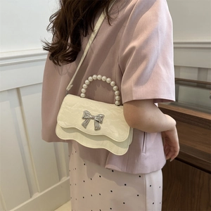 Creamy white crossbody bag with pearl handle and silver bow on a stylish model