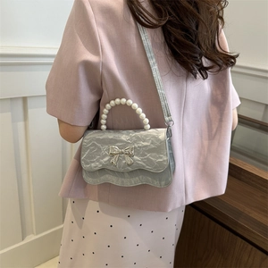 Silver pleated crossbody bag with pearl handle and metal bow decoration shown on a model