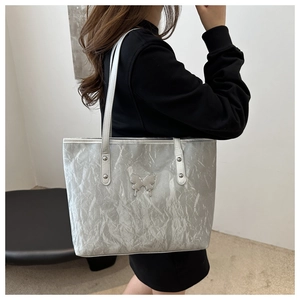 Silver tote bag with pleated texture and metal butterfly detail shown on model's shoulder