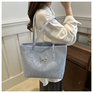 Detail of light blue pleated tote bag featuring a silver metal butterfly logo and slim strap