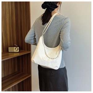 Sac bandoulière blanc avec chaîne argentée porté par un mannequin dans une pièce chaleureuse