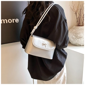 Silver metallic shoulder bag with golden bow hardware detail on modern black outfit