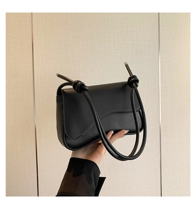 Détail du sac bandoulière noir avec rabat ondulé et embouts de sangle en métal argenté