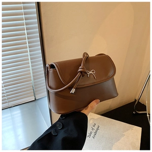 Close-up of brown leather crossbody bag featuring a silver metal bow and knotted strap detail
