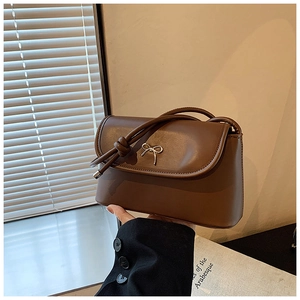 Close-up of caramel brown shoulder bag featuring golden bow detail and knotted strap