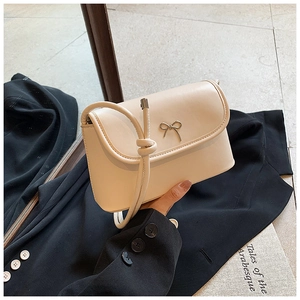 Close-up of cream crossbody bag with a golden bow metal buckle and faux leather texture