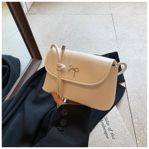 Detailed view of cream leather crossbody bag featuring a delicate gold bow metal clasp