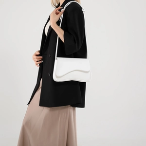 Sac bandoulière blanc minimaliste avec rabat ondulé porté sur un blazer noir élégant