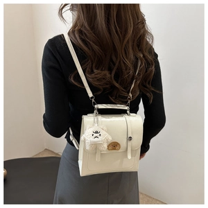 Rear view of a beige matte backpack with a plush bear charm on a minimalist background