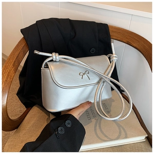 Detail of silver metallic crossbody bag with bow hardware on a textured chair