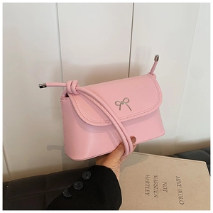 Close-up of pink leather crossbody bag featuring a silver bow buckle and knotted strap