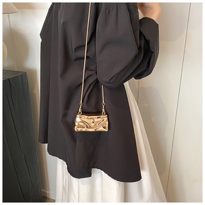 Close-up of golden metallic mini crossbody bag with wavy texture and fine chain strap