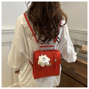 Detail of red PU leather backpack with top handle and a cute white plush bear pendant