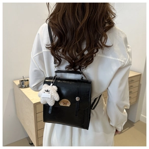 Glossy black mini bag with cartoon dog patch and plush bear charm on white dress