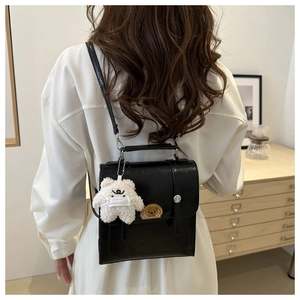 Detail of black vintage PU leather backpack featuring a white plush bear pendant decor