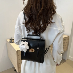Glossy black patent leather backpack with cute teddy bear charm shown on a model