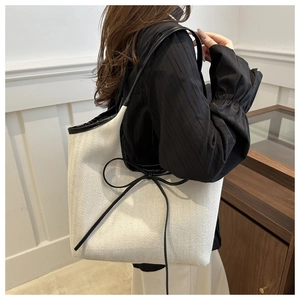 Detail of herringbone fabric tote bag with black bow decoration and slim leather shoulder strap