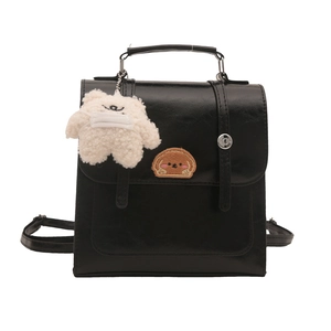 Minimalist black faux leather handbag with dog patch and plush bear charm on white background