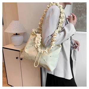 Detail of a beige tote bag with studded accents and large wavy pleated shoulder strap