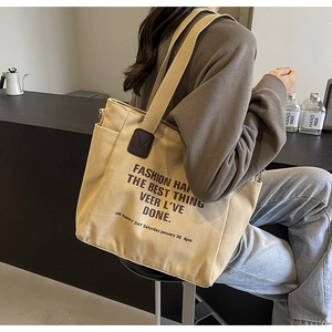 Détail du cabas en toile montrant le renfort en cuir marron et le design du texte artistique