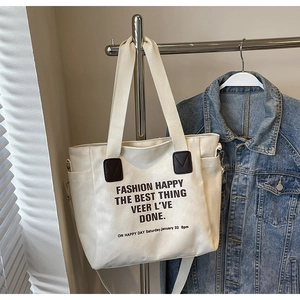 Détail du sac cabas en toile blanc cassé avec touches de cuir marron et texte noir