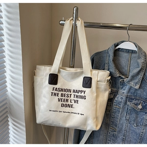 Détail du sac cabas en toile blanche montrant l'imprimé texte et les accents en cuir