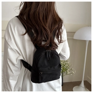 Détail d'une femme portant un mini sac à dos en nylon noir dans un cadre intérieur chaleureux
