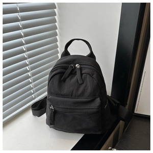 Detail view of mini black canvas backpack featuring double handles and durable zippers