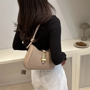 Sac baguette beige en similicuir avec boucle dorée porté à l'épaule par un mannequin