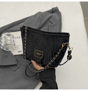Détail du sac seau noir texturé avec bandoulière chaîne dorée et nœud latéral