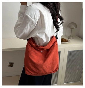 Detail view of bright orange crossbody bag with woven rope strap and silver snap button