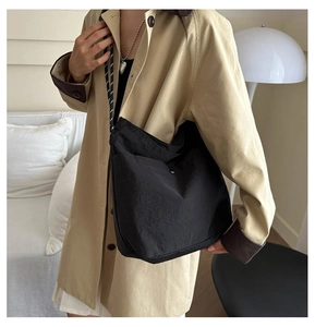 Minimalist black nylon crossbody bag with woven rope strap shown on a khaki trench coat