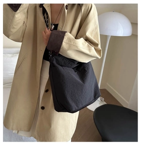 Detail of a minimalist black oversized tote bag in textured nylon with a silver heart charm