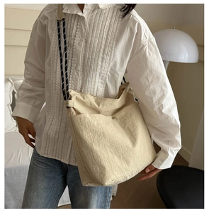 Beige canvas crossbody bag with decorative strap worn with casual outfit in soft light