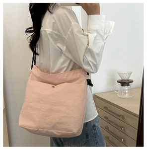 Detail of light pink canvas tote bag featuring geometric woven strap and snap pocket