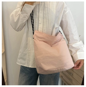 Detail of pink nylon crossbody bag featuring large capacity and black-white braided strap