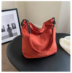 Detail of orange nylon tote bag with braided black and white rope handle and silver buckle