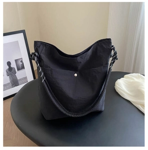 Close-up of black nylon crossbody bag featuring woven rope strap and silver snap button