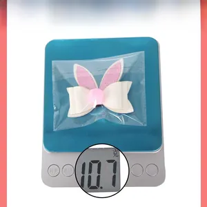 Dettaglio molletta orecchie di coniglio con glitter rosa su bilancia che pesa 10,7 grammi