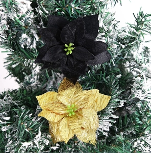 Close-up of black velvet and gold glitter Christmas flowers on snowy pine branches