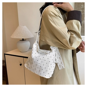 Detail of white polka dot shoulder bag featuring delicate lace trim and soft fabric