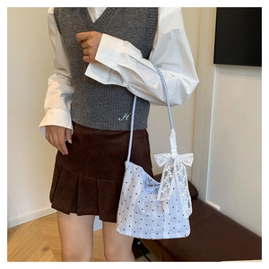 Detail of light blue polka dot shoulder bag featuring a large white lace bow charm