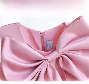 Detail of a pink satin girl's dress featuring a large bow on the round neckline