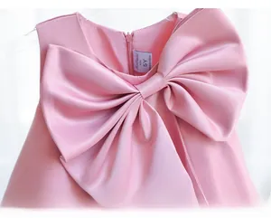 Detail of a pink satin girls dress featuring a large layered bow and smooth silk texture