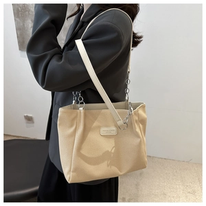 Detail of canvas tote bag with leather strap, metal chain, and logo patch on front